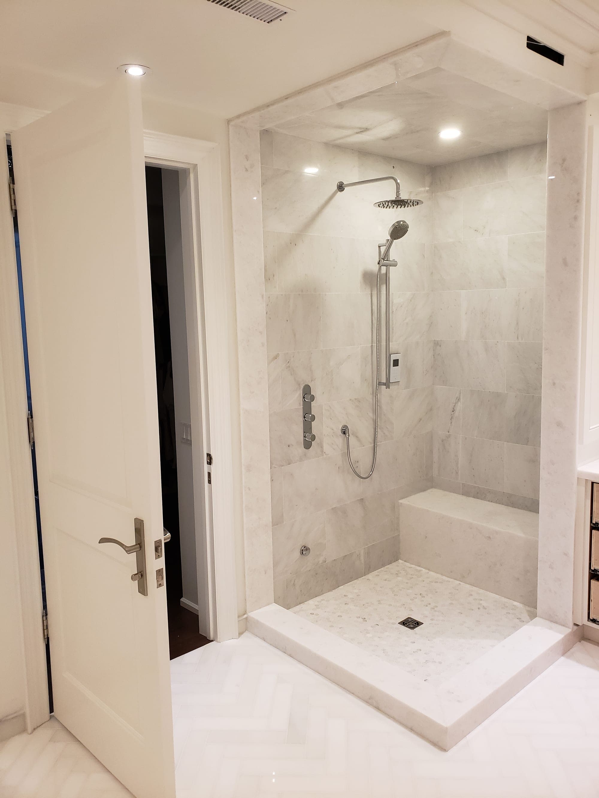 Wide view of finished marble walk-in shower with herringbone marble floor leading in