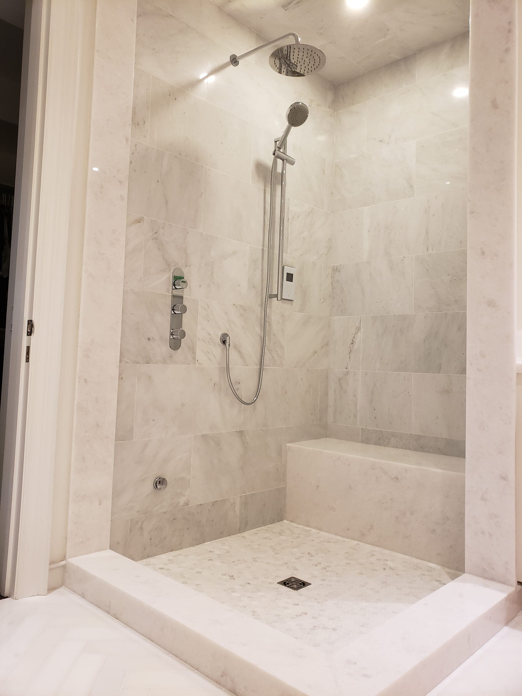 Master bathroom walk-in shower with Carrara marble subway tile, marble bench seat, and hex marble mosaic floor — installed by Blue Tile & Marble in Toronto